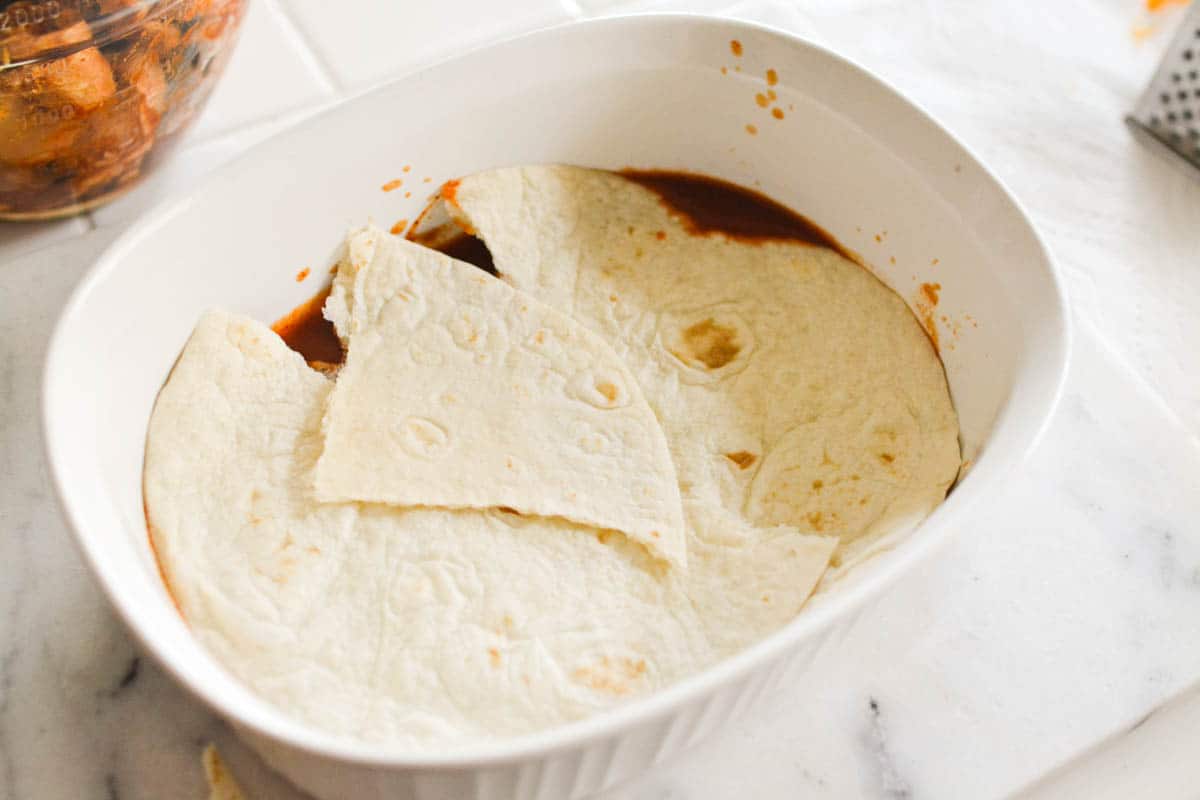 Baking dish with enchilada sauce and layer of tortillas.
