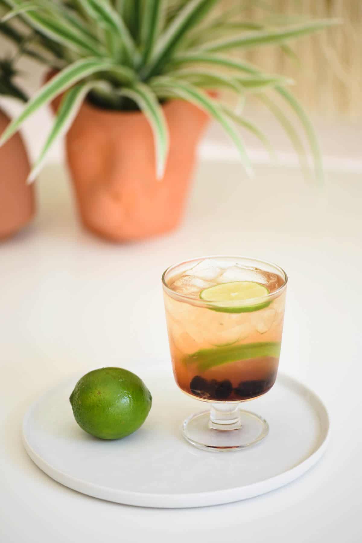 Footed cocktail glass next to a lime on a table.