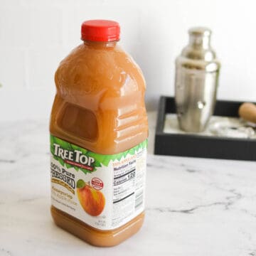 Close up of a bottle of Apple Juice with a cocktail shaker in the background.