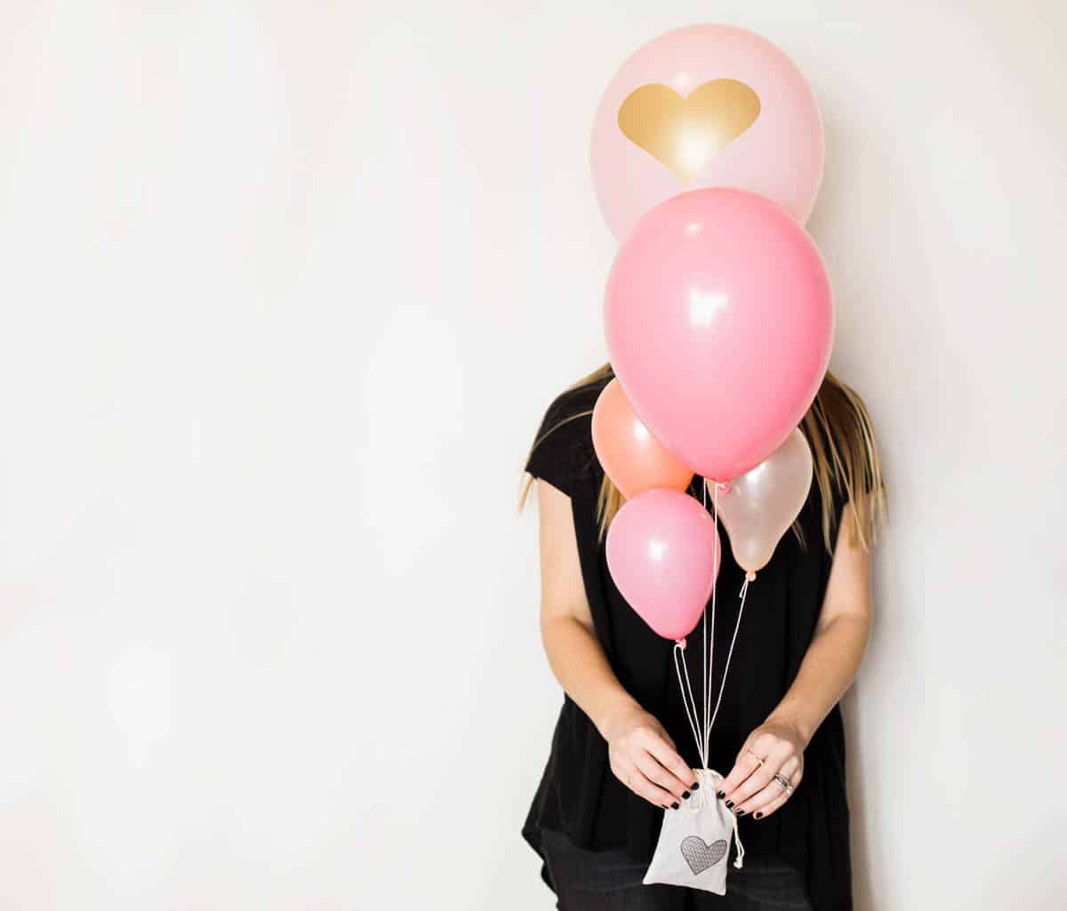 Woman holding a lavender sachet balloon weight attached to a pink balloon bouquet for Valentine's Day.