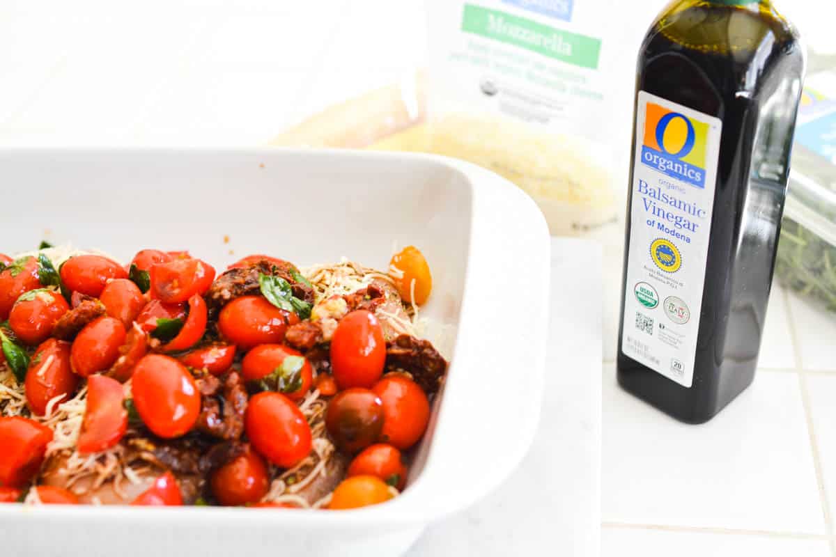 A bottle of balsamic vinegar next to a baking dish ready to go in the oven.