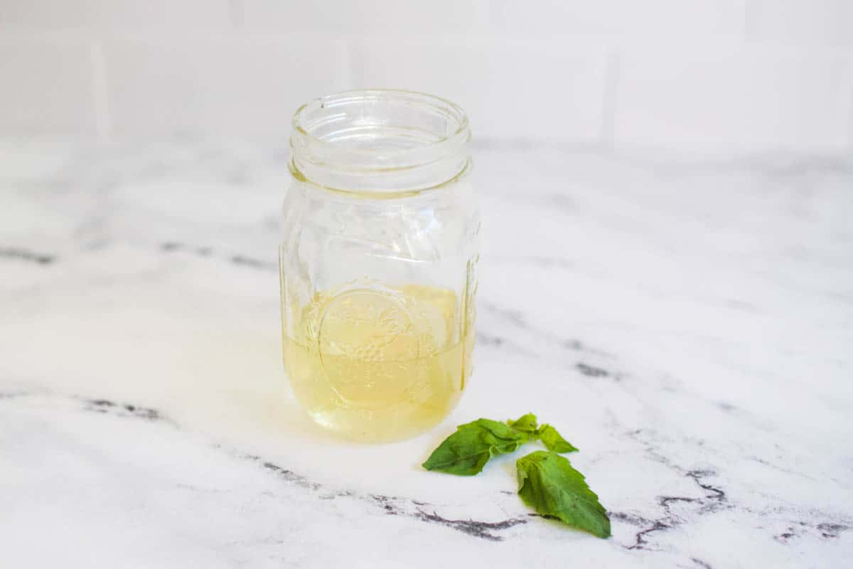 jar full of basil syrup for cocktails sitting on white marble counter 