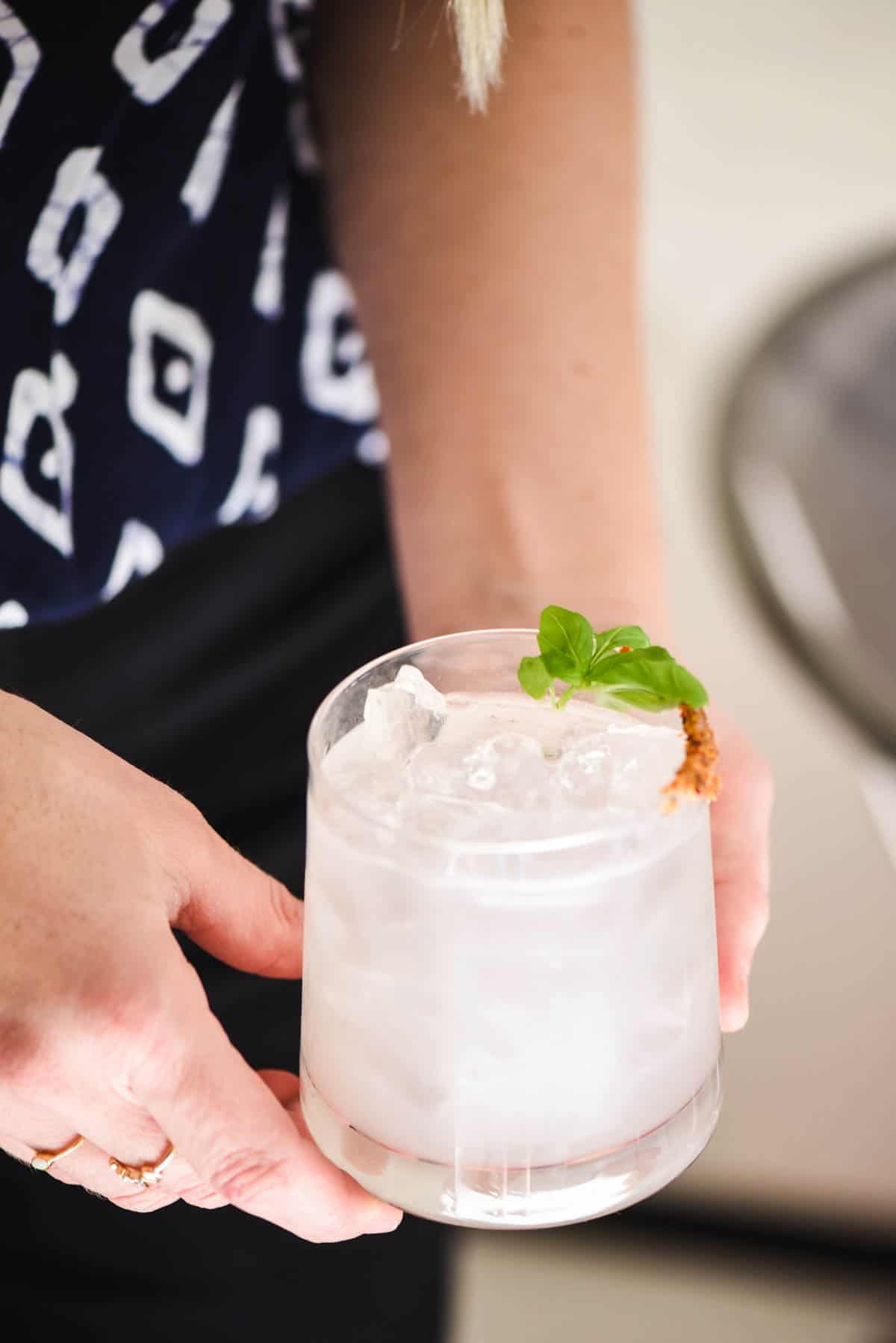 Close up of a basil margarita recipe garnished with fresh basil held by a woman. 