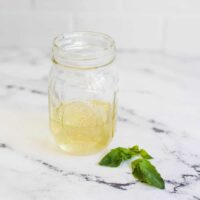 jar of basil syrup with extra basil leaves on counter