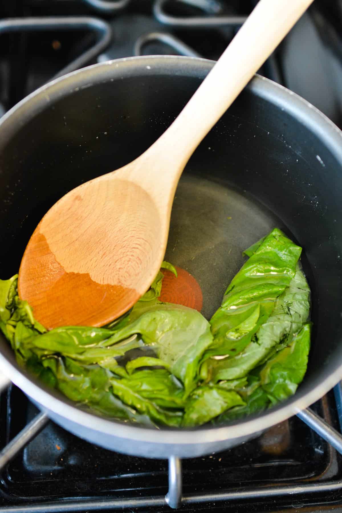 basil in sauce pan on the stove with wooden spoon 