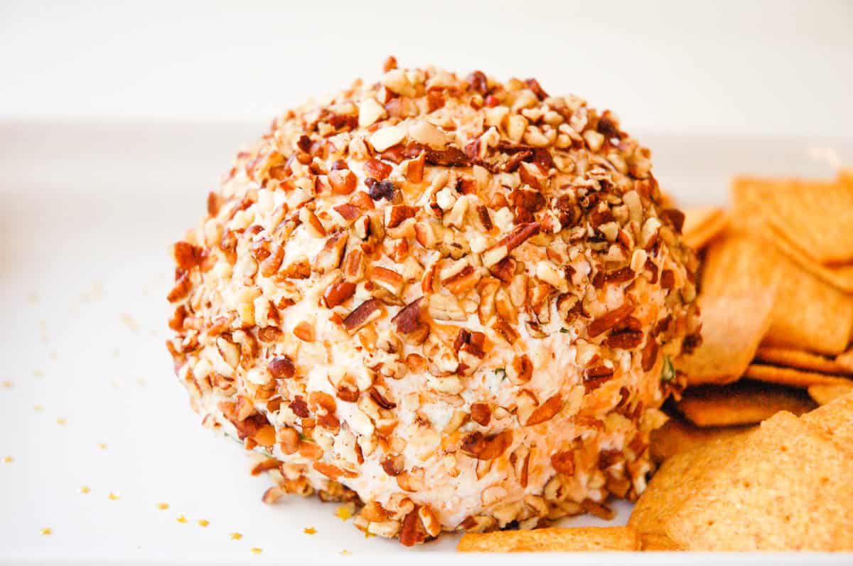 A cheese ball rolled in pecans next to some crackers.