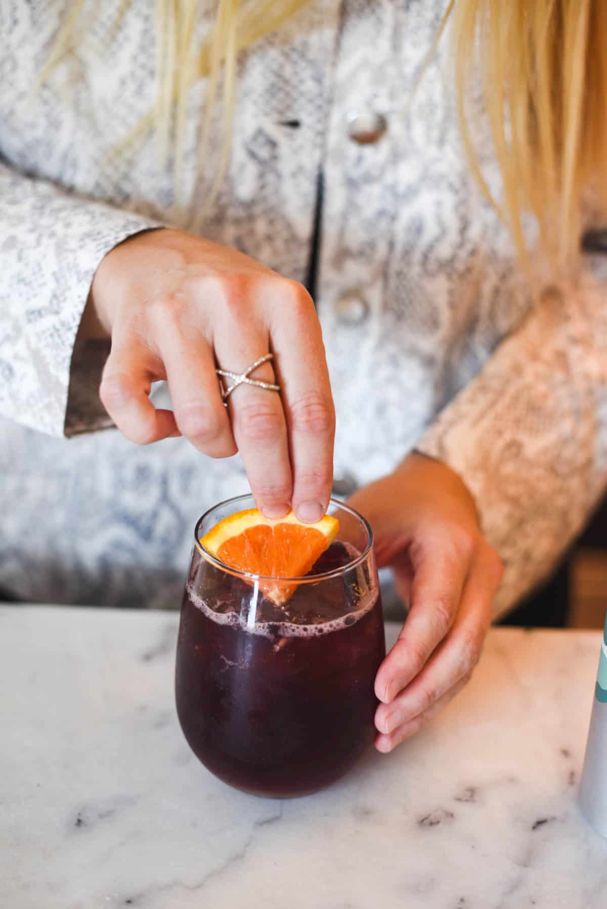 Woman adding a piece of orange to a red wine cocktail.