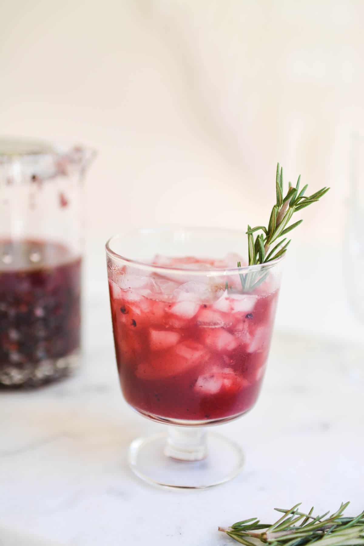 Close up of pink cocktail with a rosemary garnish.