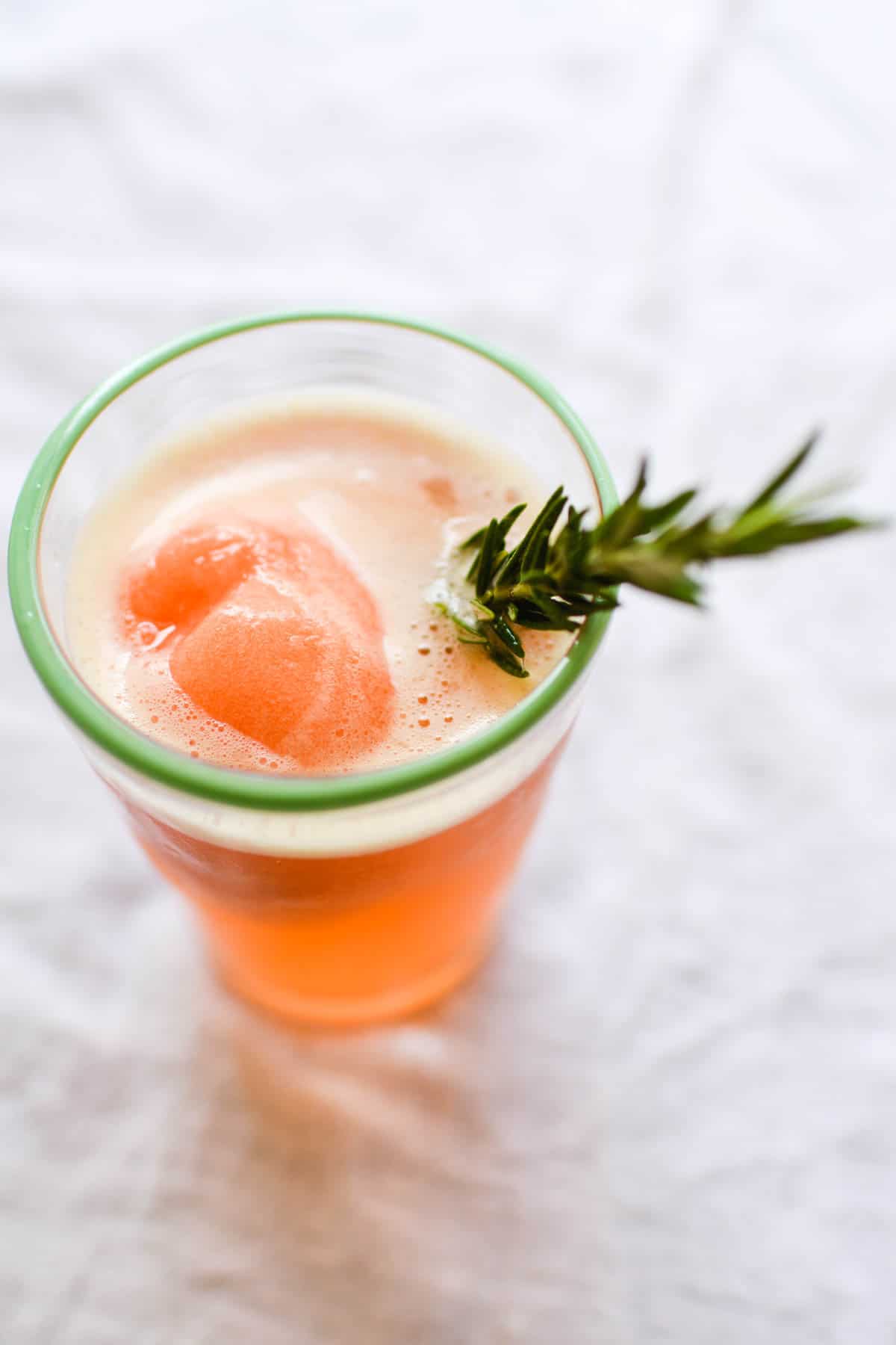 Close up of a cocktail with sorbet and a rosemary sprig.