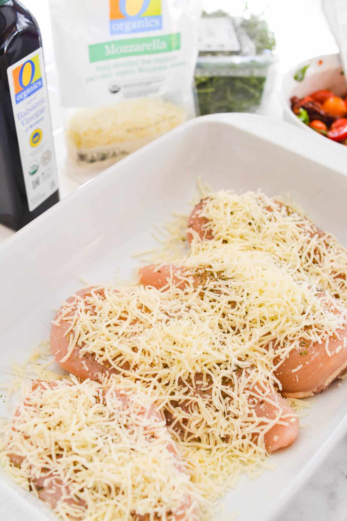 Raw chicken breasts in a baking dish topped with shredded mozzarella cheese.