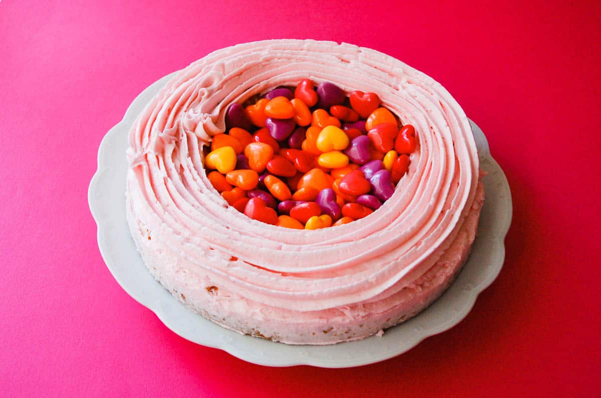 A cake with a ring of icing on top and heart candies in the middle