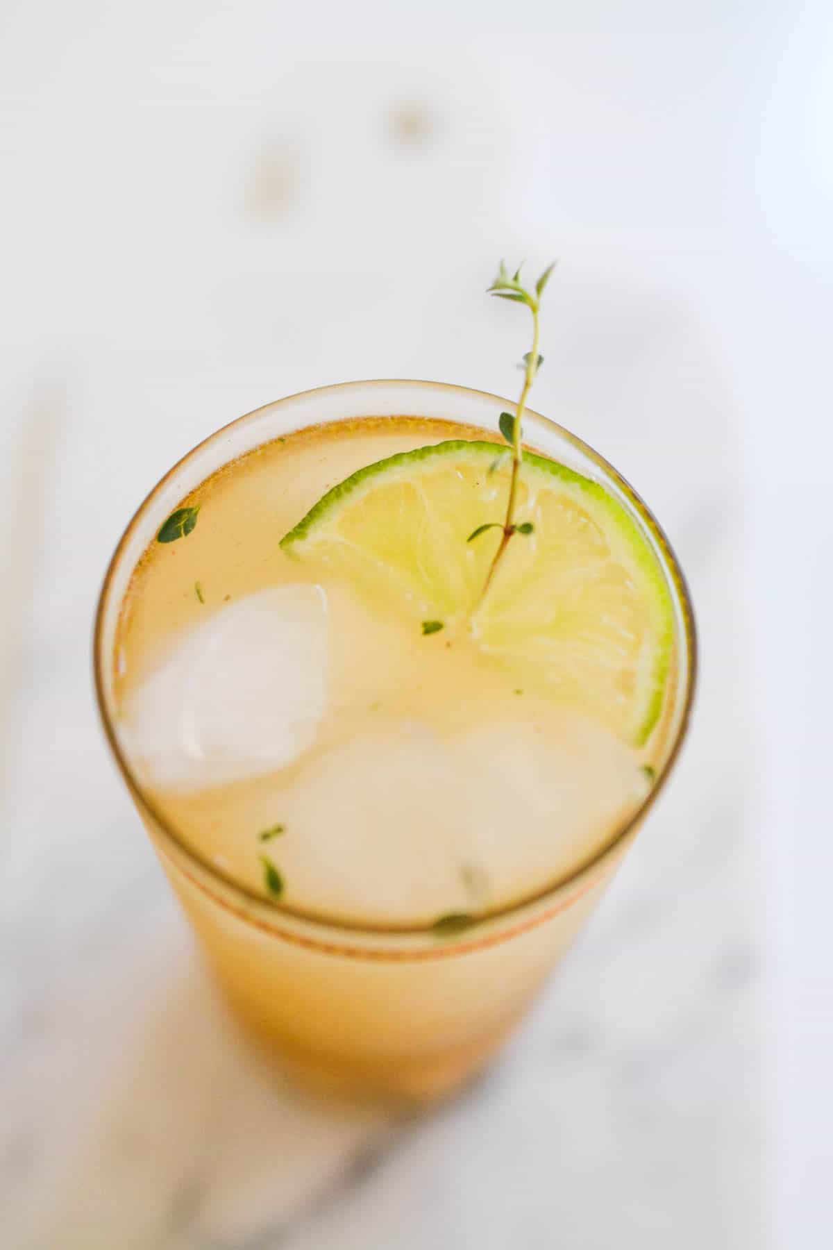 Close up of a cocktail in a glass with thyme and lime garnish.