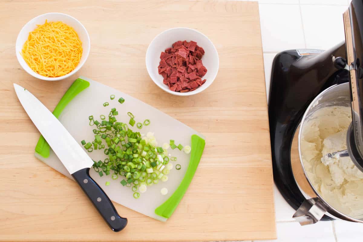 Cutting board with green onions and chopped dried beef next to a stand mixer.
