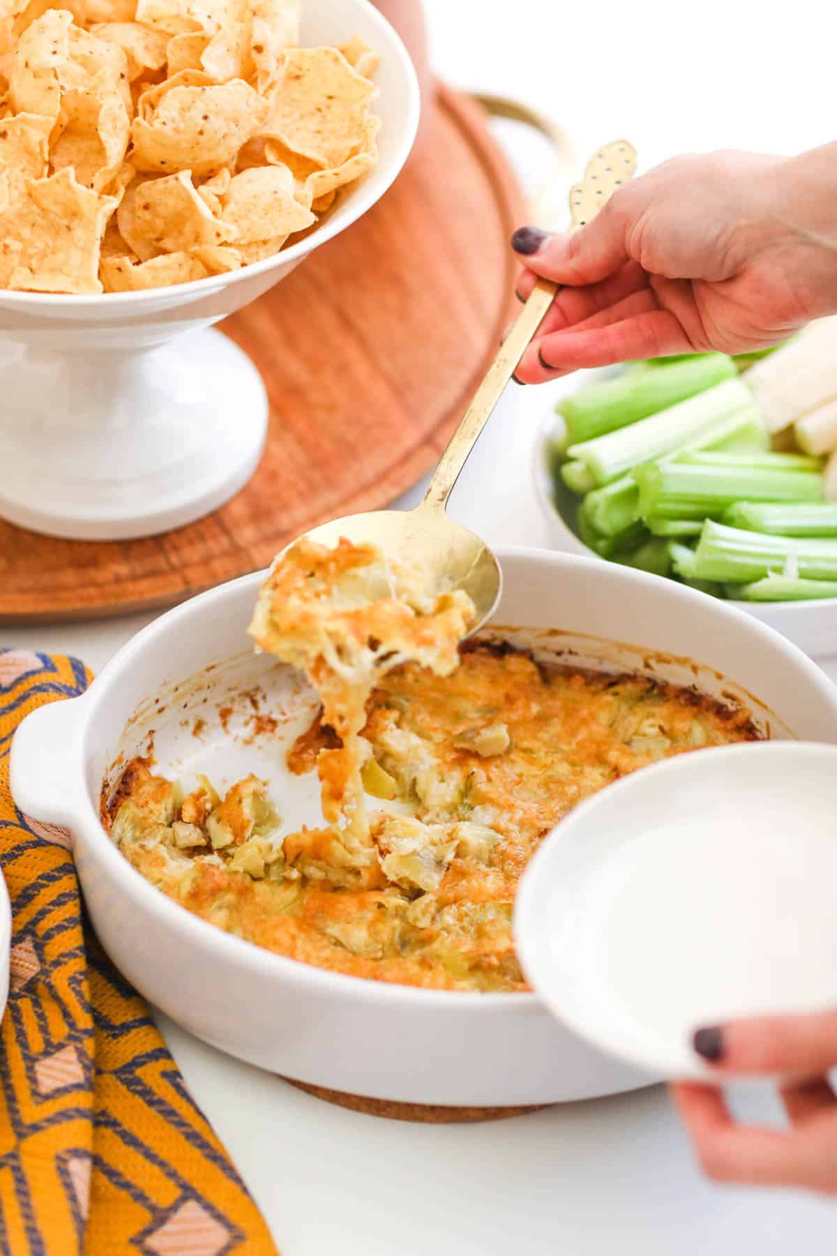 Scooping hot artichoke dip onto a small appetizer plate.
