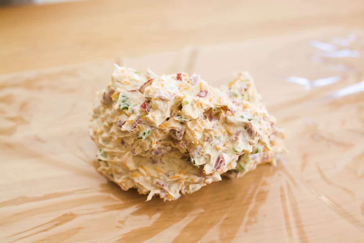 Cream cheese with dried beef and other ingredients to make a cheese ball on a piece of plastic wrap.