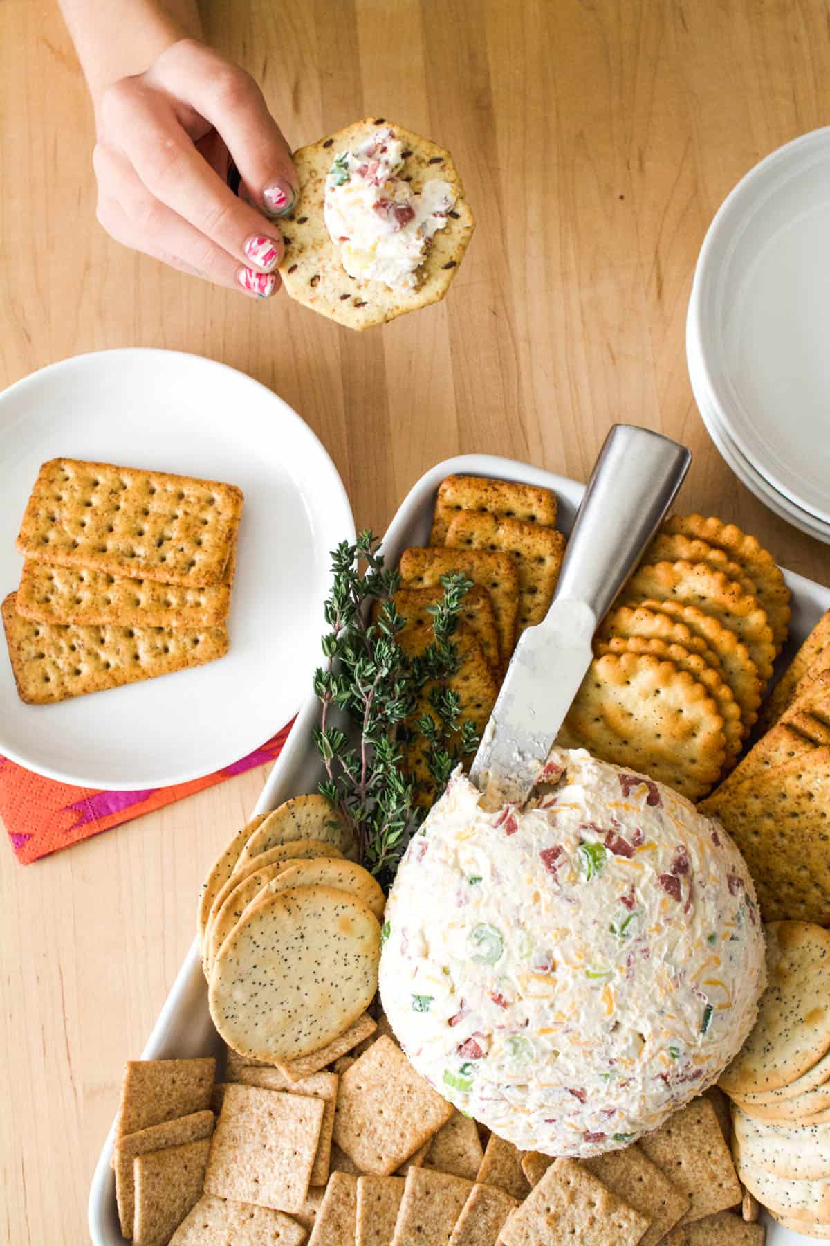 overhead shot of a chipped beef cream cheese ball with a serving knife and kid holding a cracker.