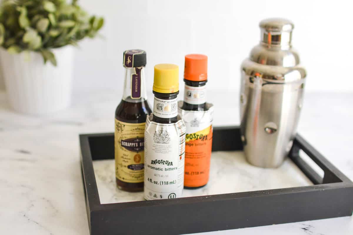 Bottles of bitters on a tray next to a cocktail shaker.