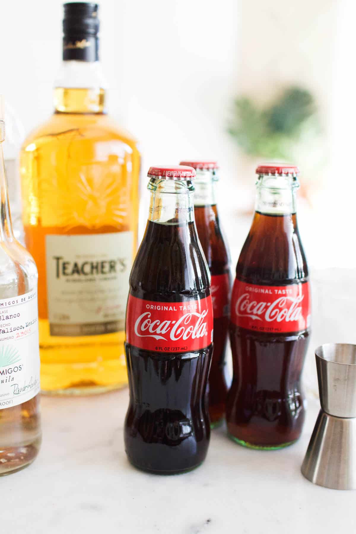 Coke bottles on a counter next to a bottle of scotch and tequila.