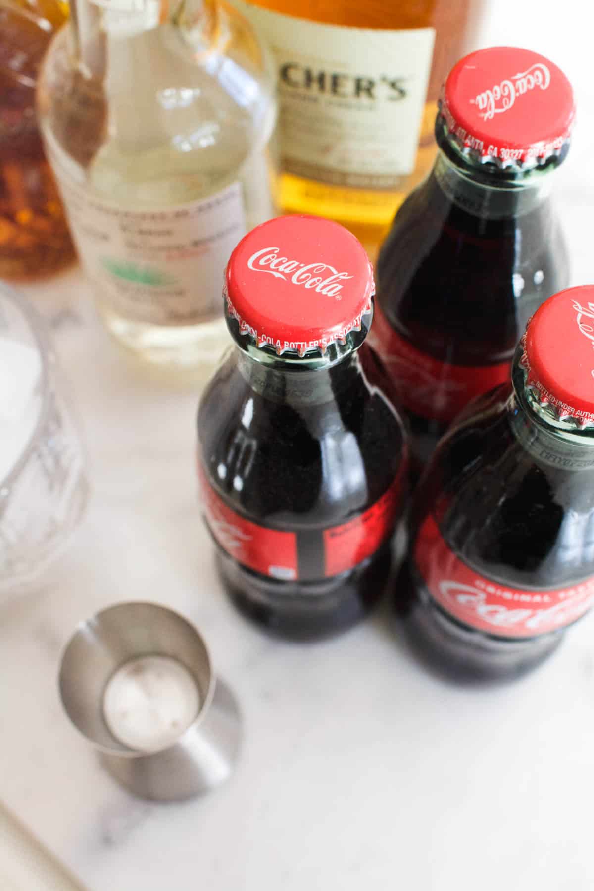 Close up of Coke bottles on a table next to bar tools and bottles.