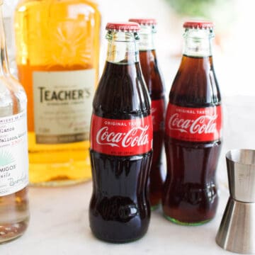 Close up of Coke bottles on a counter next to bottles of liquor.