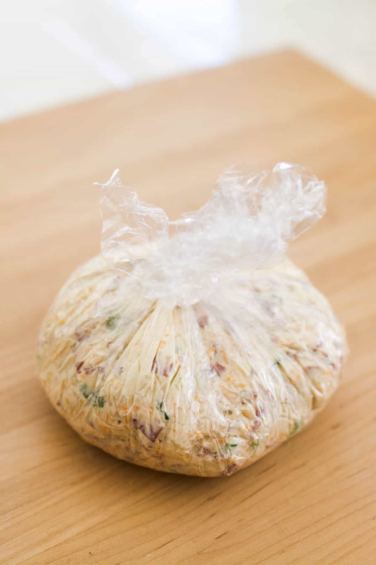 Cream cheese ball with dried beef wrapped up in plastic wrap on a counter.