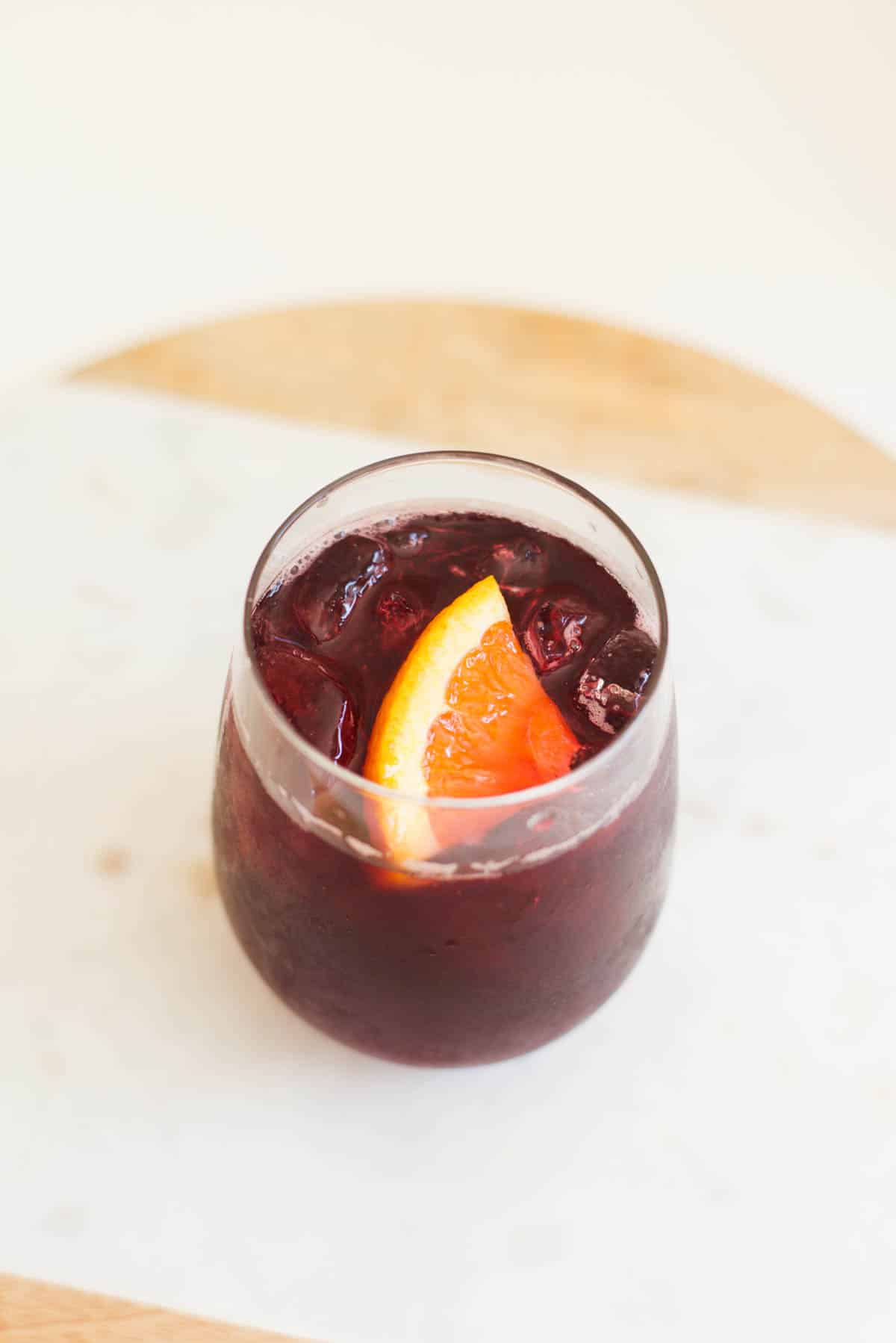 Close up of the top of a cocktail made with red wine with a small piece of orange as a garnish.