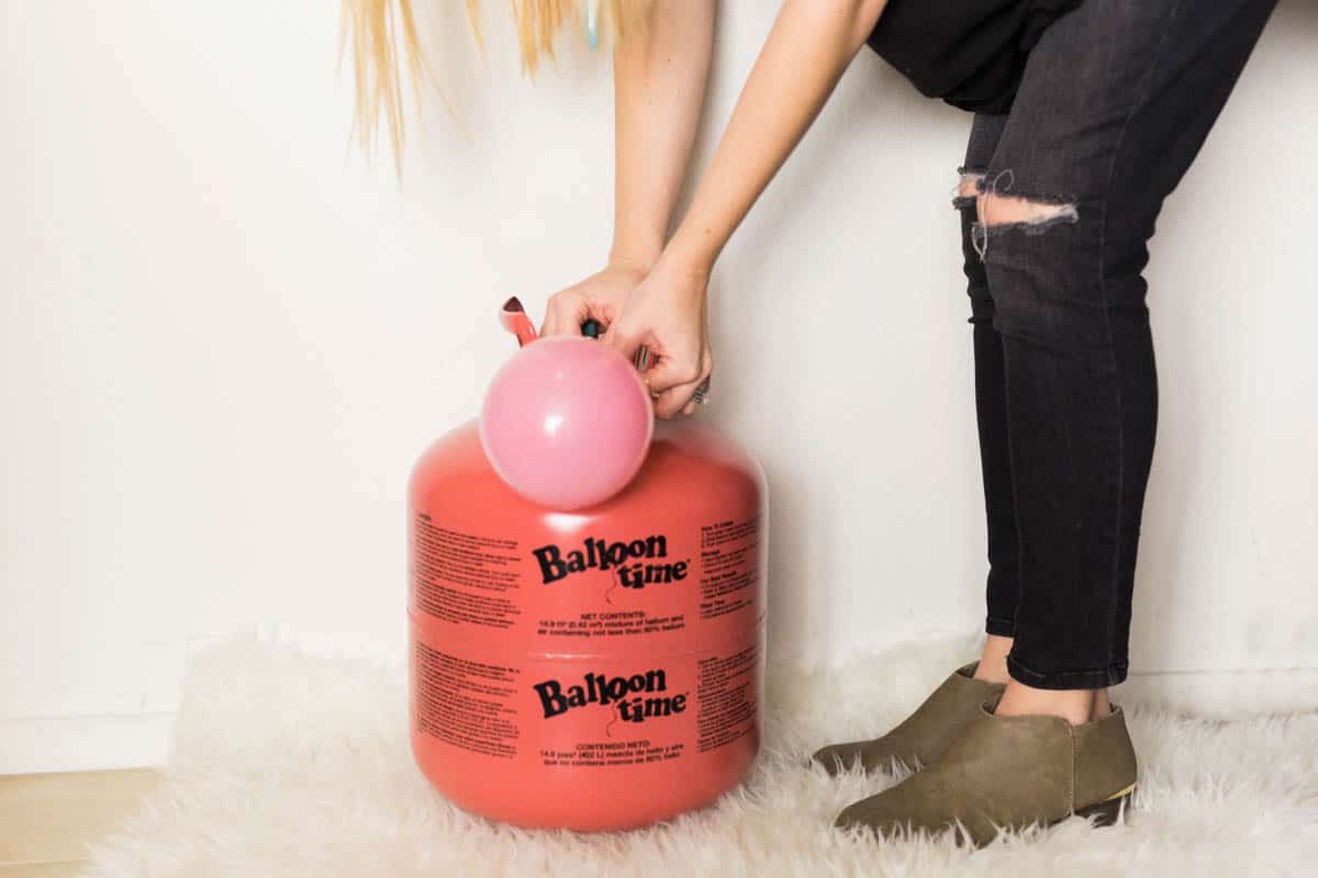 Woman using a helium tank to blow up a pink balloon.