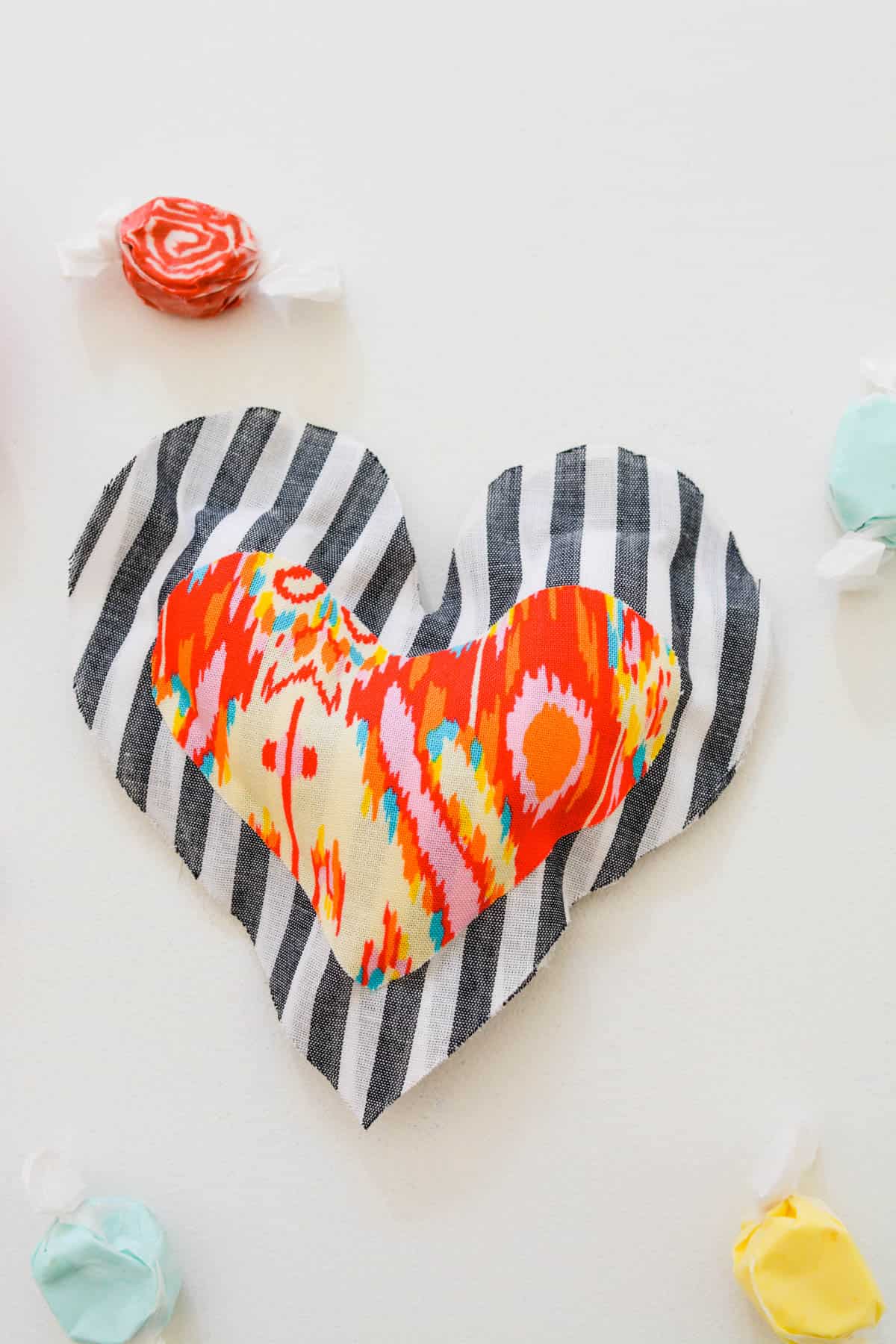 A DIY heart pillow made of fabric and shaped like a heart with some candy next to it.