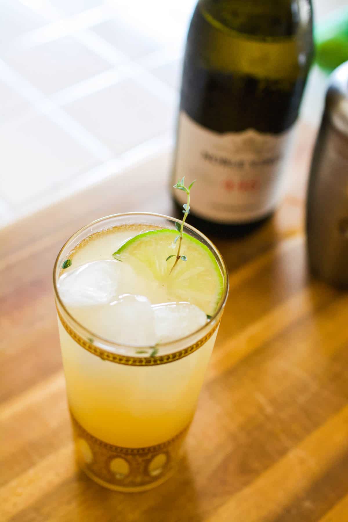 cocktail in a tall glass on a cutting board next to a bottle of wine.