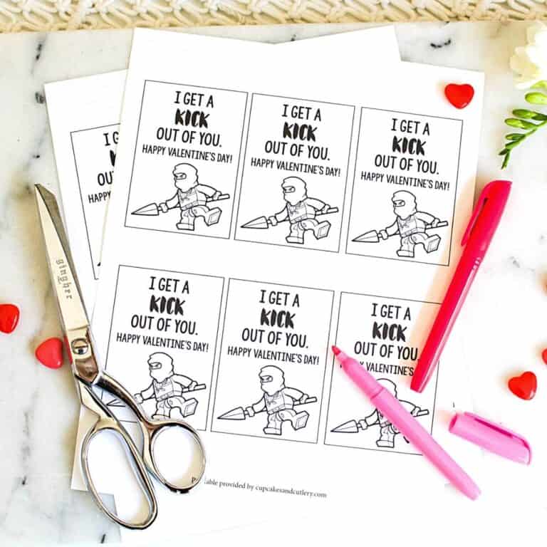 Top down view of a sheet of printable lego ninjago valentines, markers and scissors.