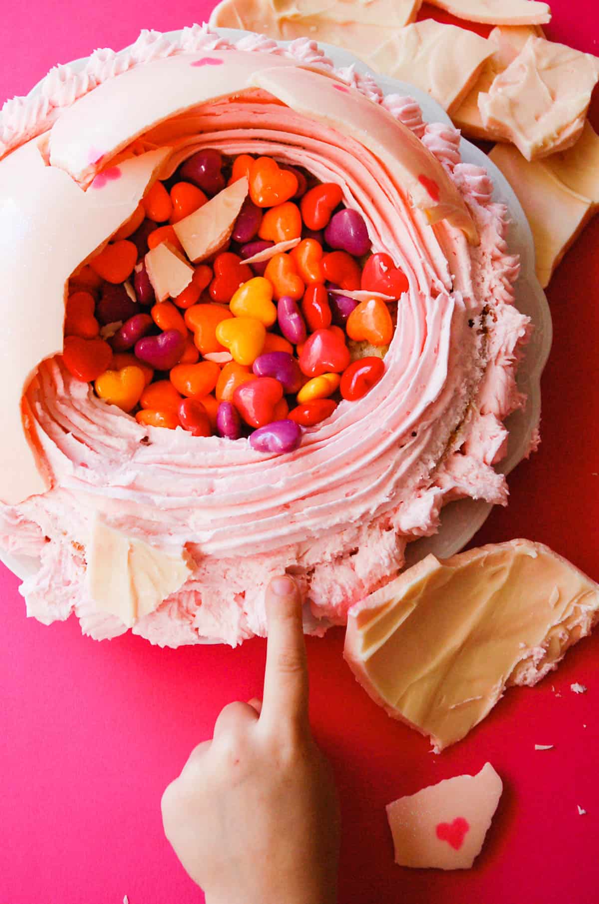 A kid reaching for frosting on a cake filled with candy.