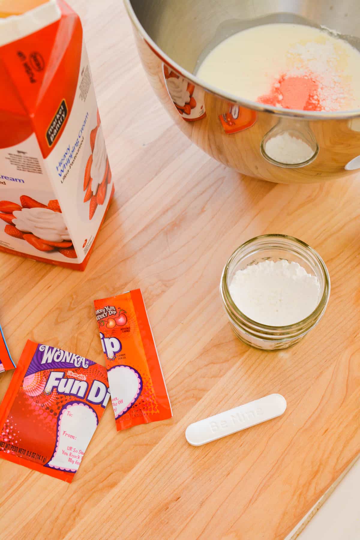 A counter with a mixing bowl, Fun Dip Candy and heavy whipping cream.