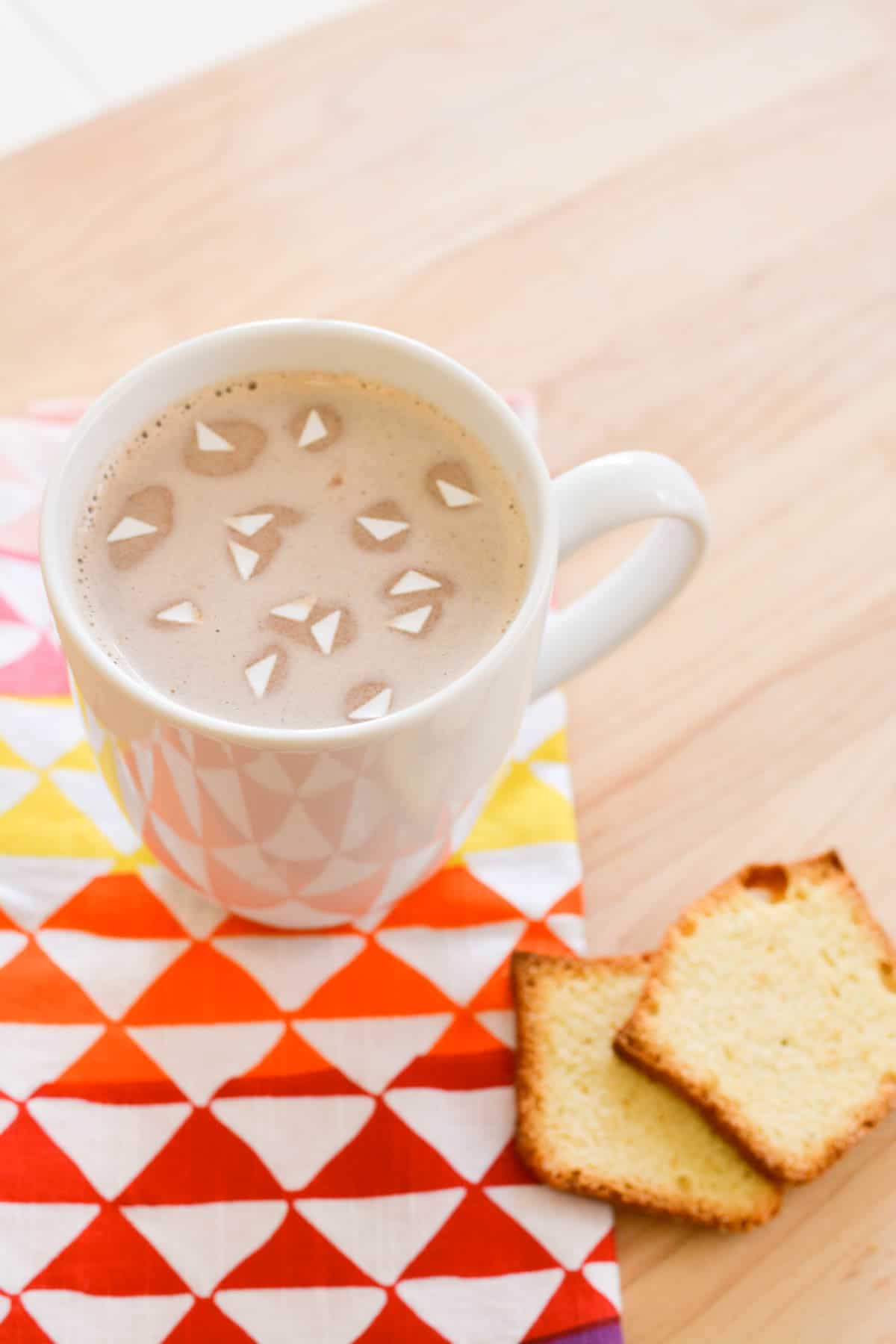 A mug of hot chocolate on a napkin topped with triangle shaped edible confetti.