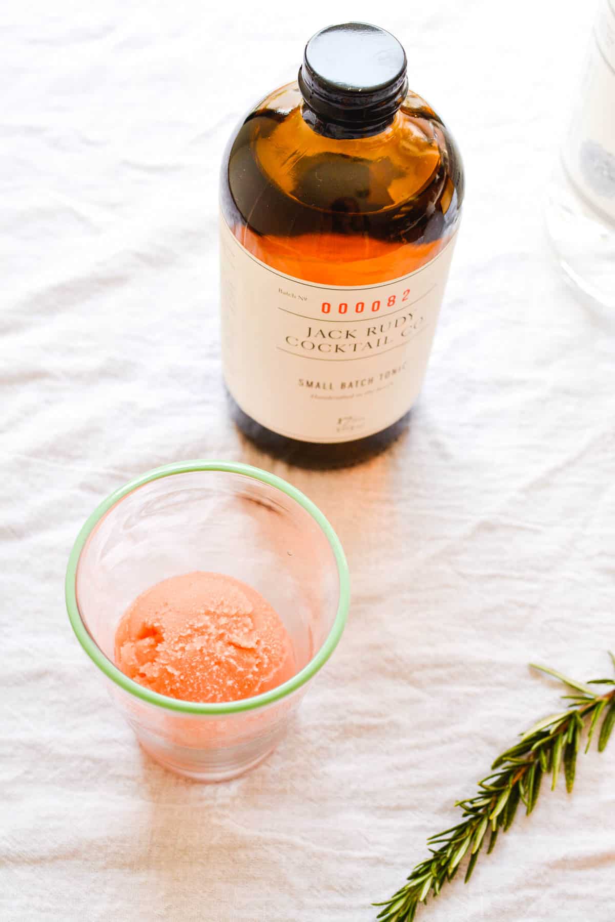 A cocktail cup holding blood orange sorbet next to a bottle of tonic.