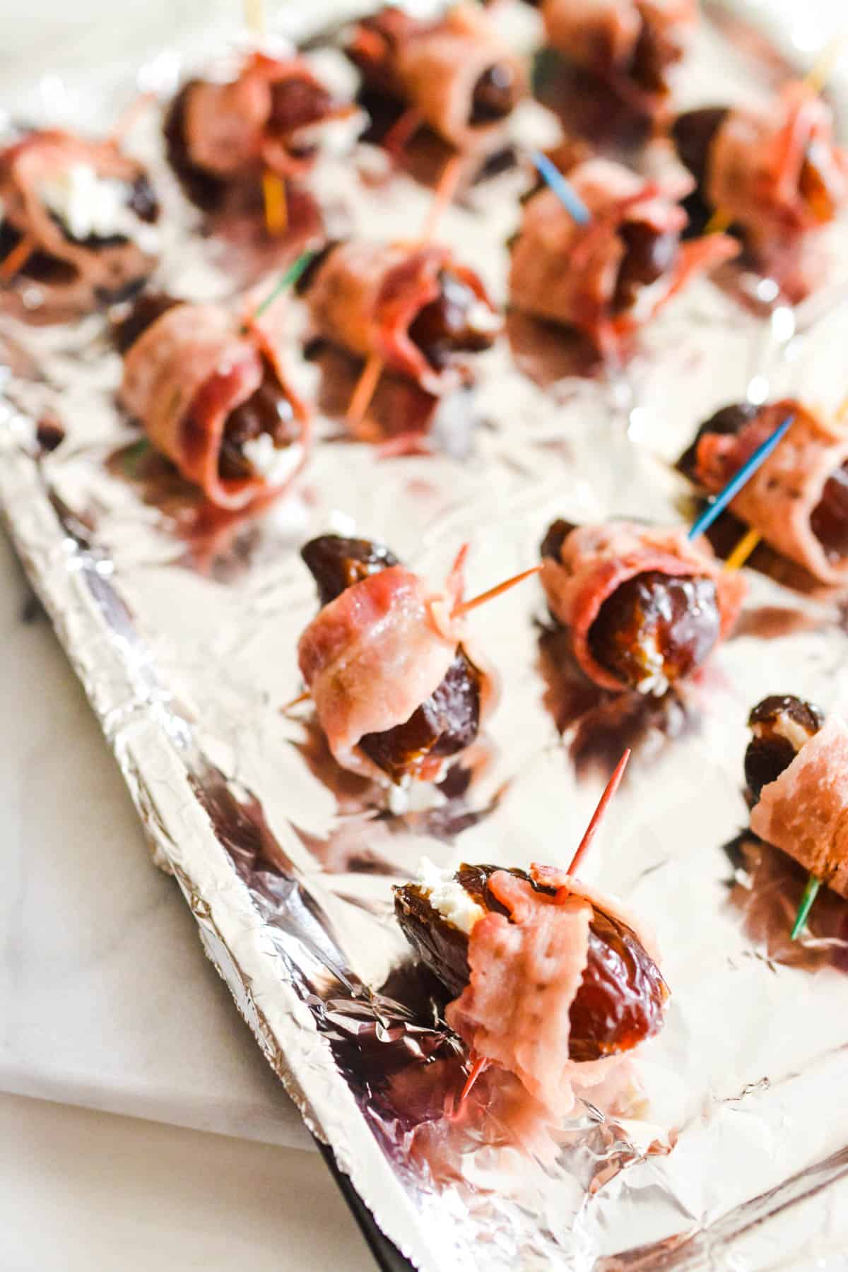 Bacon wrapped dates with toothpicks in them on a foil covered baking sheet.