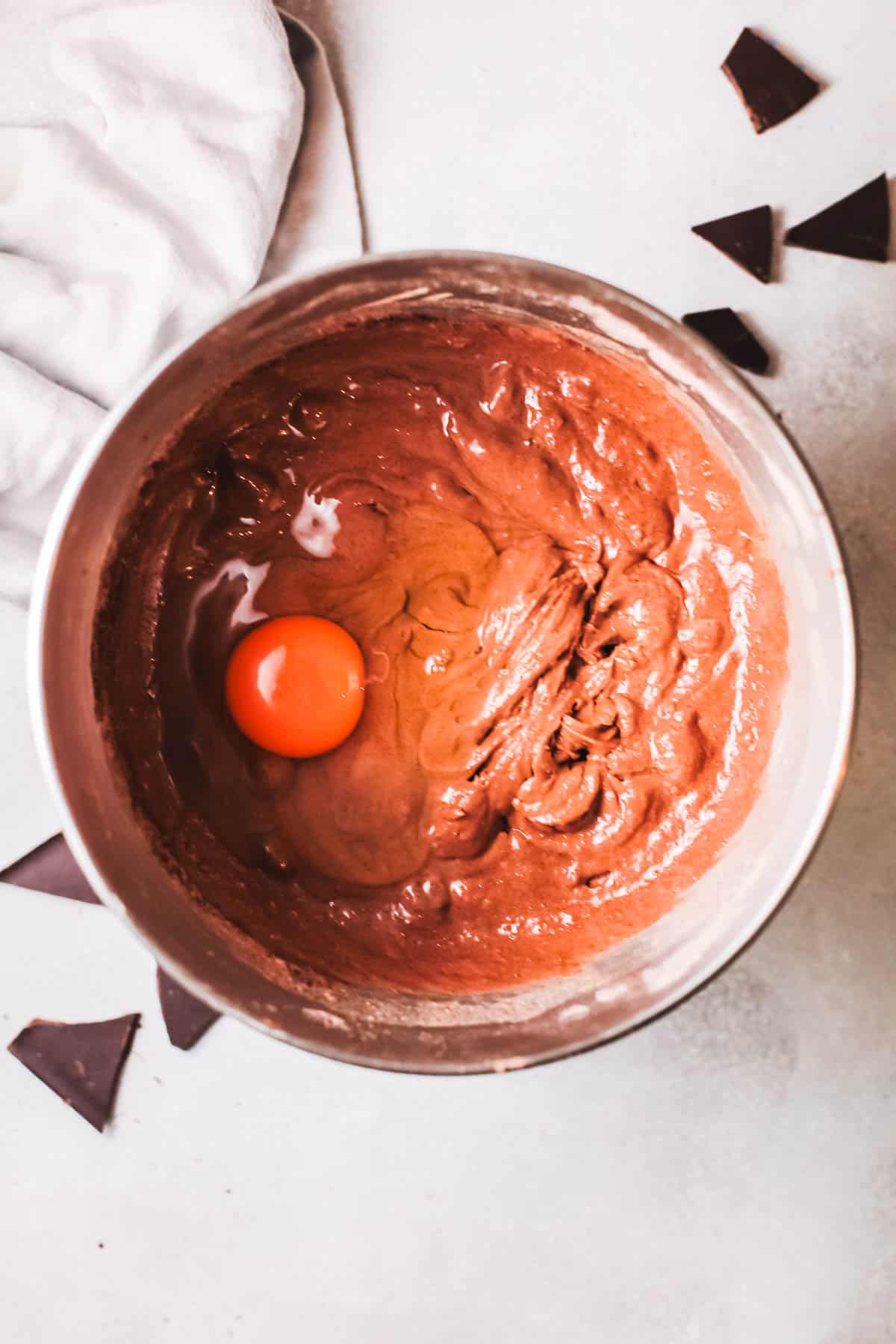 A bowl on a counter with cake batter and a whole egg broken into it. 