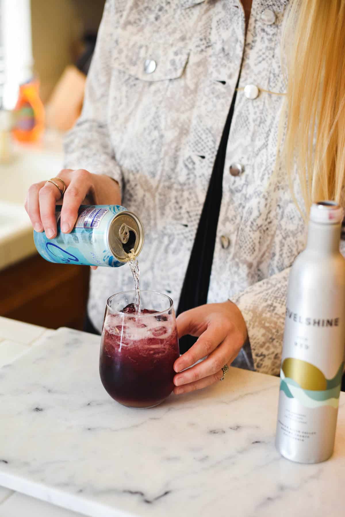Woman adding club soda to a stemless wine glass.
