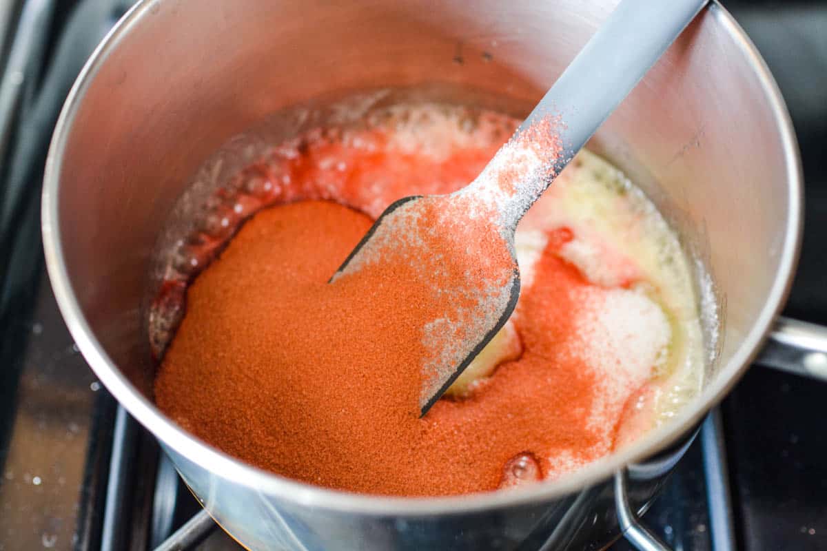 Pink Jello powder in a suace pan with a spatula.