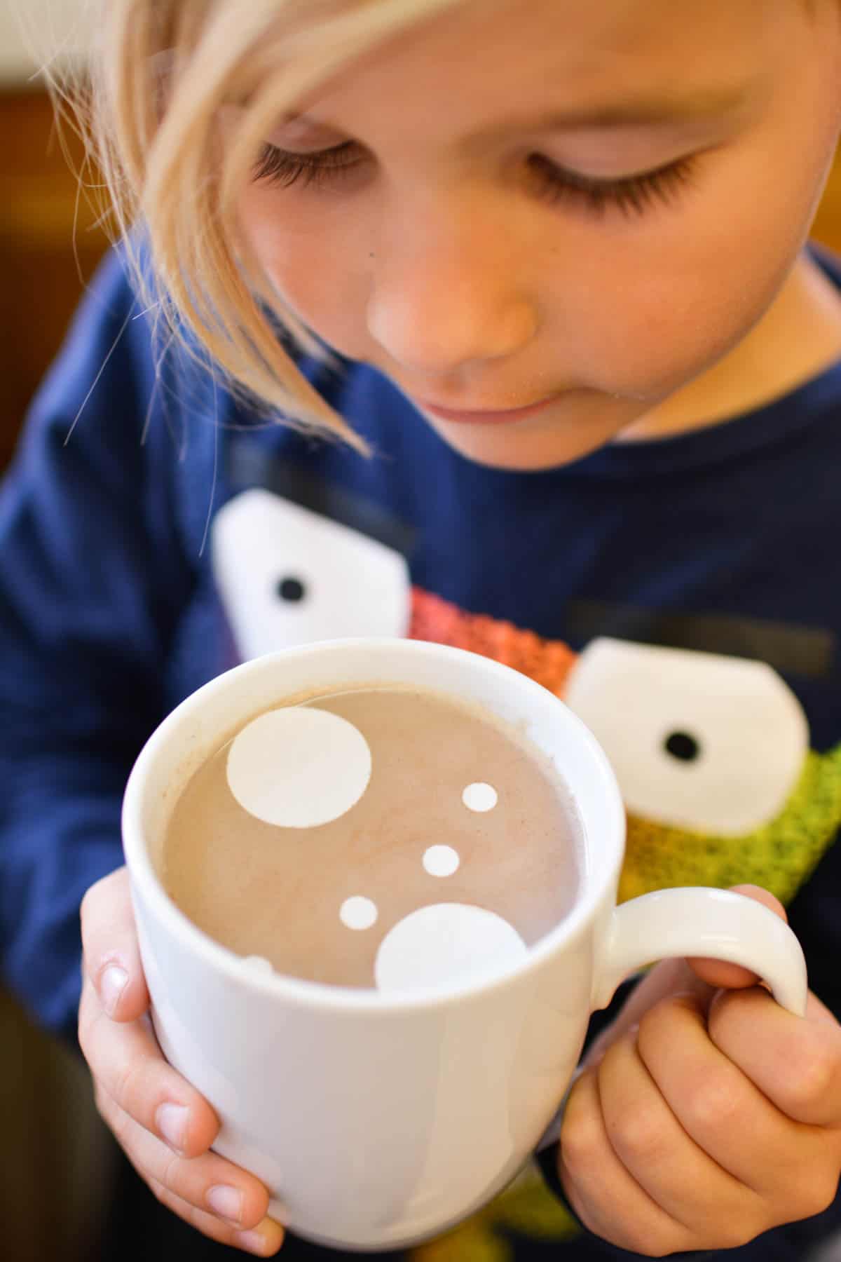 Kid holding a mug of hot chocolate topped with edible confetti polka dots.