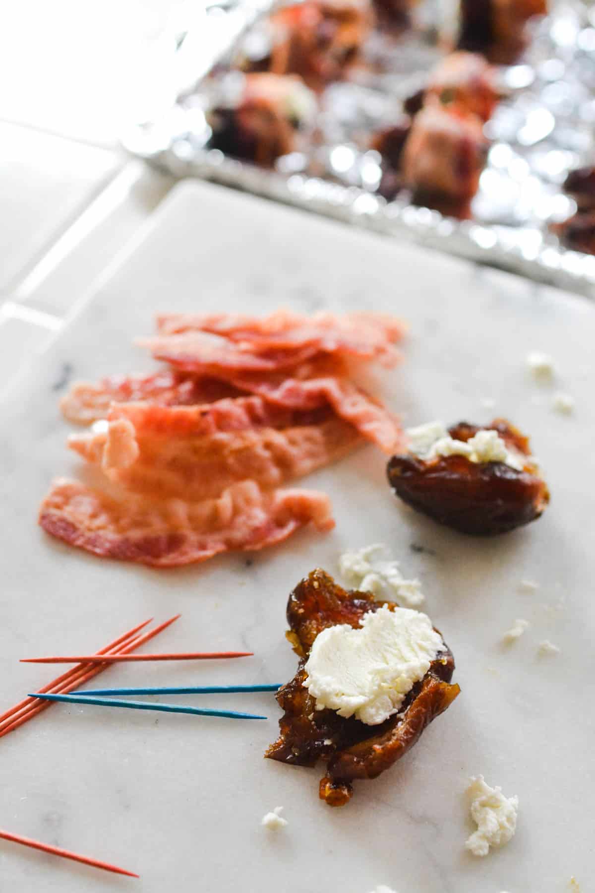 Bacon and dates on a cutting board, one stuffed with goat cheese