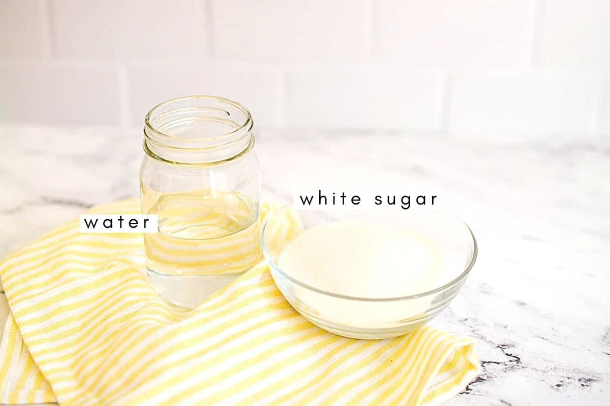 Close up of a jar of water and a small bowl of white sugar on a table.