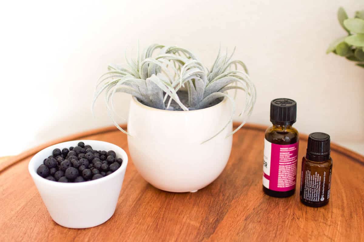 Lava rocks in a bowl next to a faux succulent planter and bottles of essential oils.