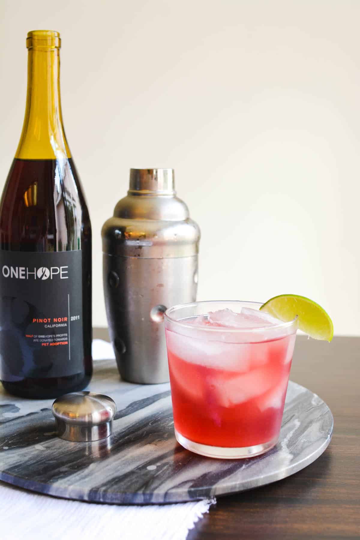 A red wine cocktail with tequila on a tray next to a bottle of red wine and a cocktail shaker.