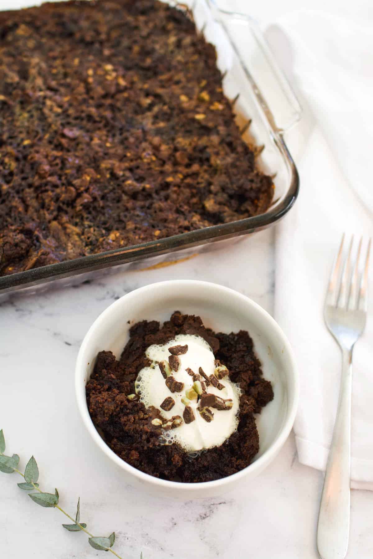 A serving of a chocolate peppermint dump cake in a small white bowl next to the baking dish.