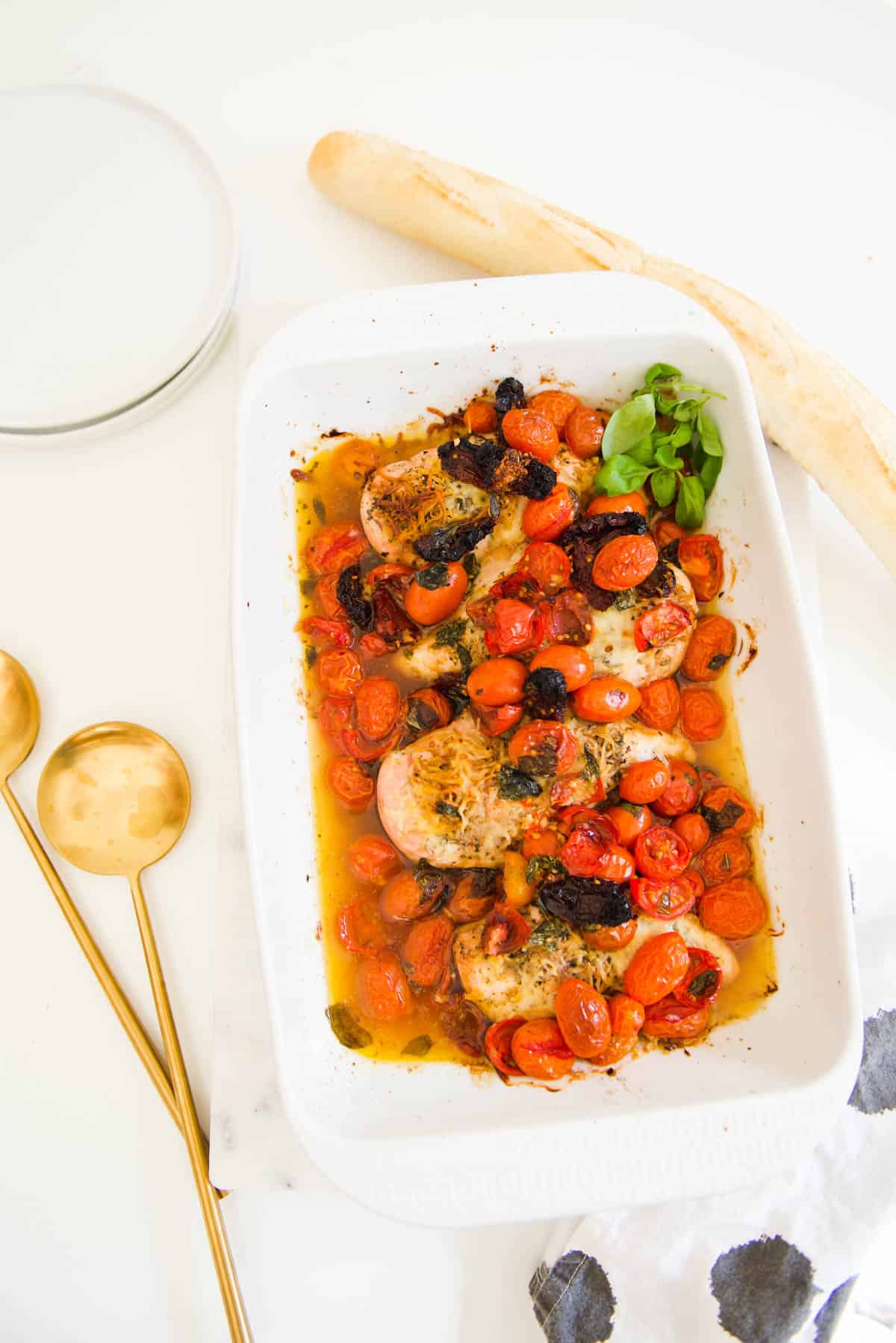 A baking dish with tomatoes on top of chicken breasts on a table. 