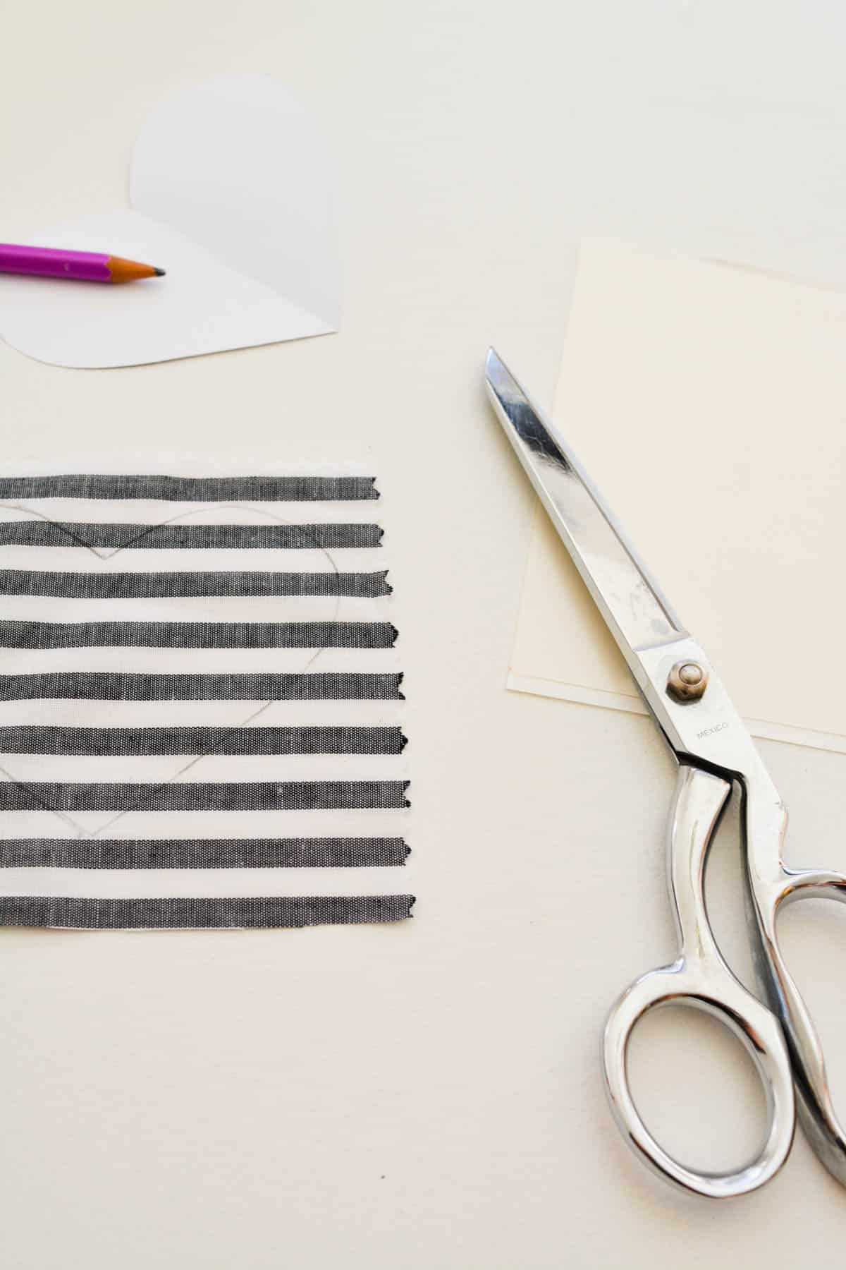 A piece of fabric with a heart shape drawn on it on a table next to some scissors.