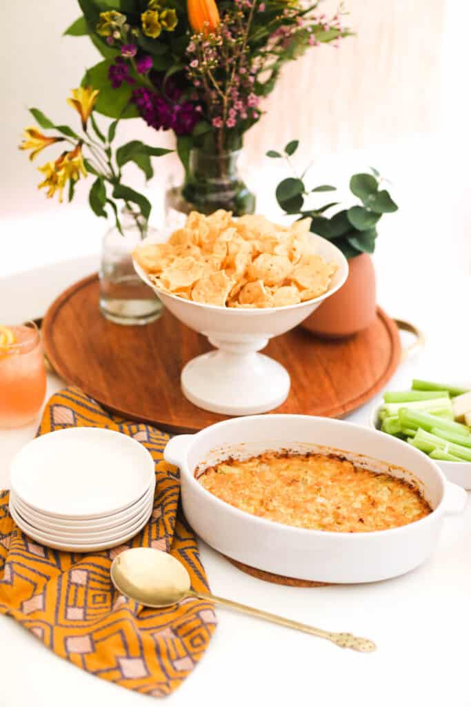 Hot Artichoke Dip on a party table next to a bowl of tortilla chips.