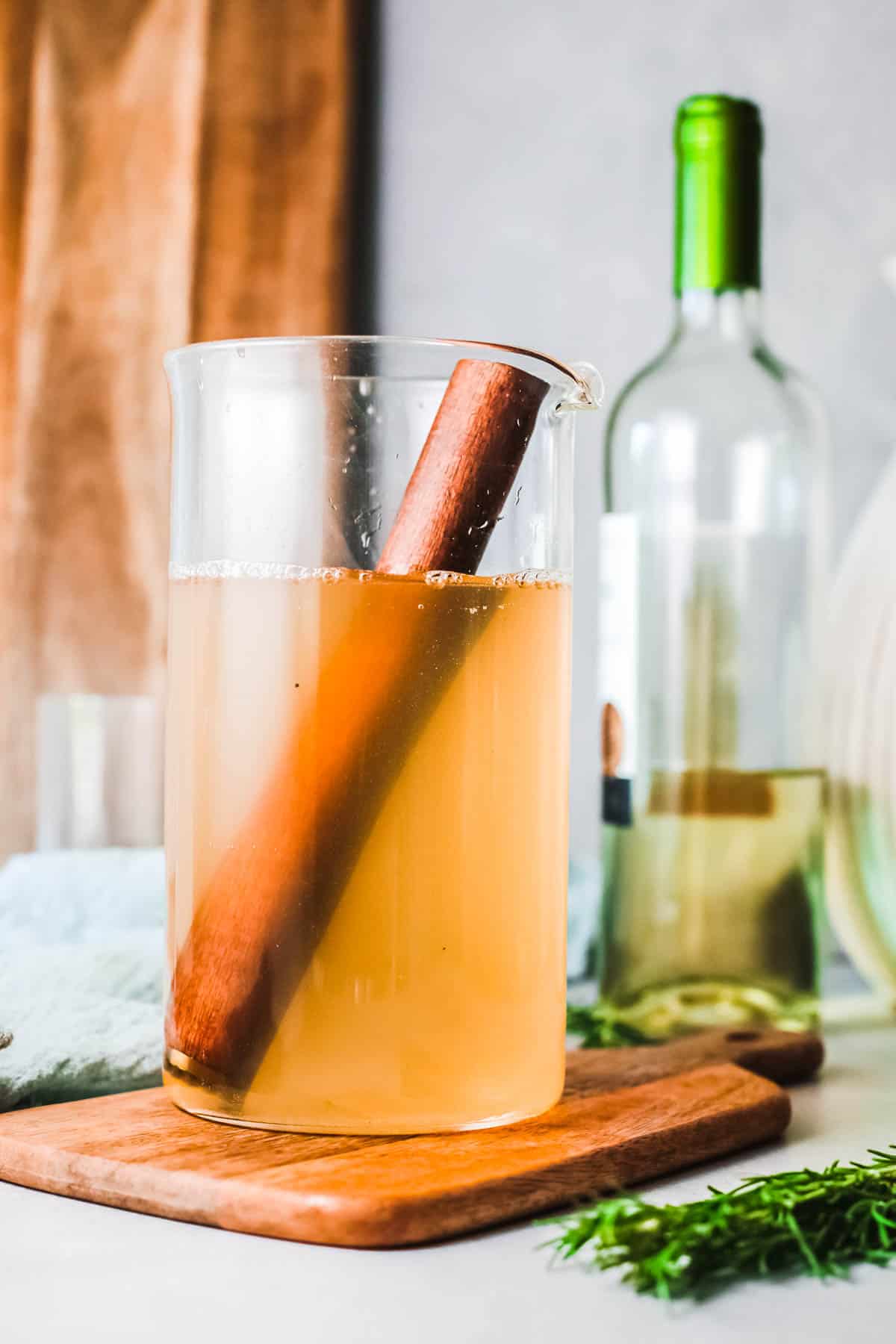 A glass cocktail pitcher on a wooden board on a table with a wooden muddler in the amber colored sangria.