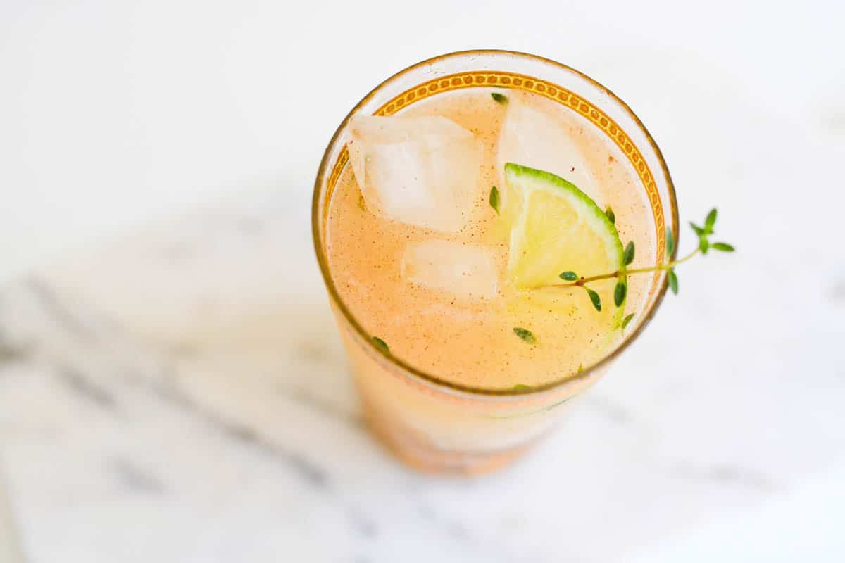 Top view of a cocktail glass on a table with a lime and thyme garnish.