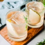 Close up of cocktail glasses each with a pear slice and rosemary sprig.